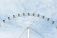 weißes Riesenrad mit blauen Kabinen vor leicht bewölktem Himmel
