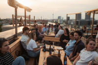 Menschen sitzen auf der Dachterasse des Berliner diffferent Büros im Abendlicht. Im Hintergrund ist Berlin, der Fernsehturm und die Spree zu sehen.